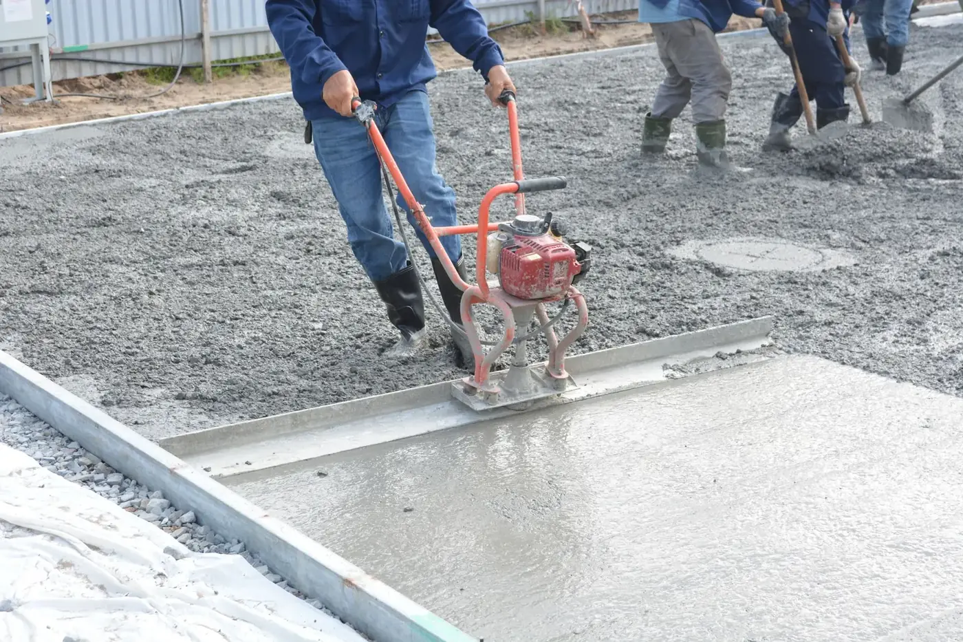 Worker leveling a freshly poured concrete slab with a power screed